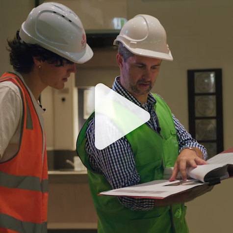 Two people with hardhats and high visibility vests looking over work plans
