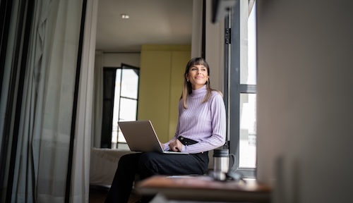 Woman sitting with a laptop on her lap looking out the window.